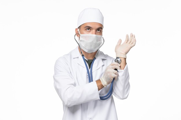 Vista frontal médico de sexo masculino en traje médico y con máscara debido a covid- comprobando su pulso en la pared blanca enfermedad covid- enfermedad por virus pandémico