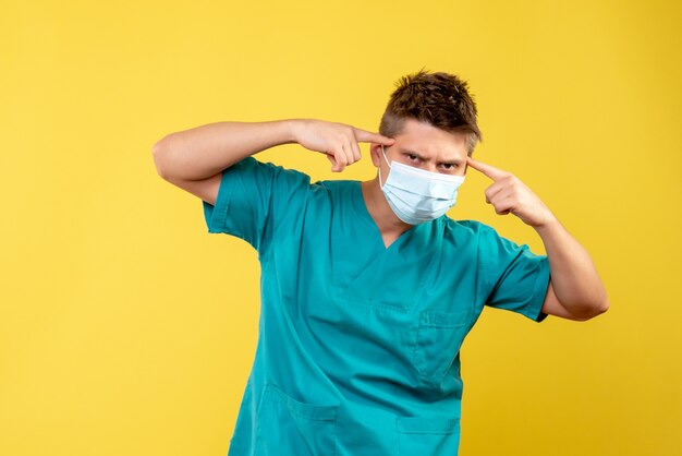 Vista frontal del médico de sexo masculino en traje médico y máscara estéril en la pared amarilla