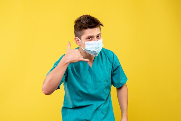 Vista frontal del médico de sexo masculino en traje médico con máscara estéril en la pared amarilla