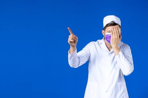 Vista frontal del médico de sexo masculino en traje médico y máscara púrpura sobre azul