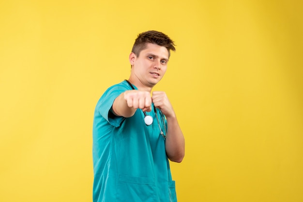 Vista frontal del médico de sexo masculino en traje médico mostrando su puño en la pared amarilla