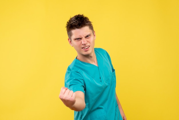 Vista frontal del médico de sexo masculino en traje médico en la pared amarilla