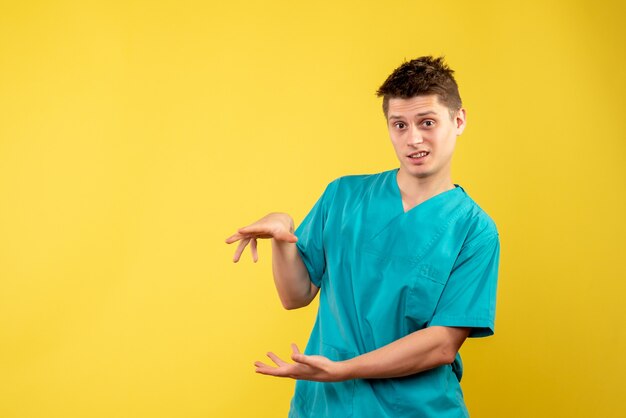 Vista frontal del médico de sexo masculino en traje médico en la pared amarilla