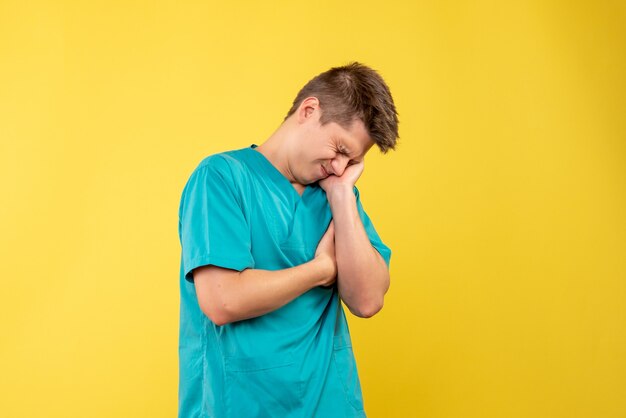 Vista frontal del médico de sexo masculino en traje médico en la pared amarilla