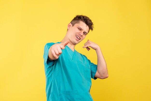 Vista frontal del médico de sexo masculino en traje médico en la pared amarilla