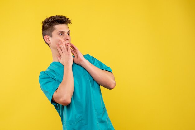 Vista frontal del médico de sexo masculino en traje médico en la pared amarilla