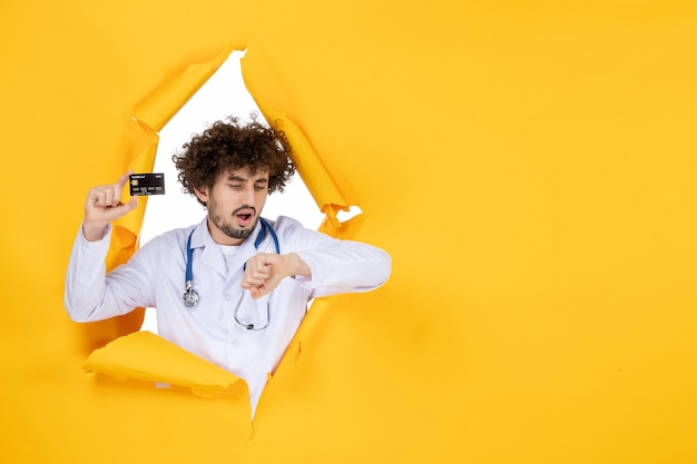 Vista frontal médico de sexo masculino en traje médico con tarjeta bancaria en el hospital de virus de medicina de salud médico de color amarillo rasgado