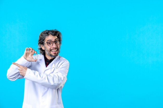 Vista frontal médico de sexo masculino en uniforme médico sosteniendo pequeño frasco en el azul