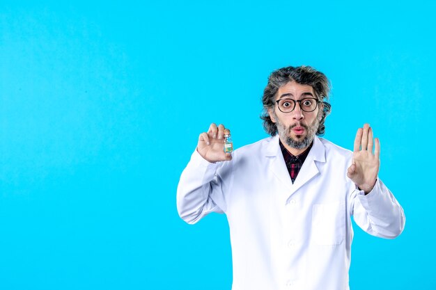 Vista frontal médico de sexo masculino en uniforme médico sosteniendo pequeño frasco en el azul