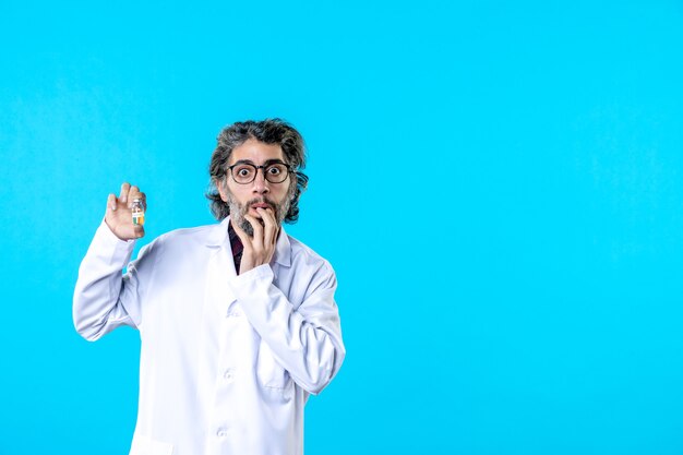 Vista frontal médico de sexo masculino en uniforme médico sosteniendo pequeño frasco en el azul