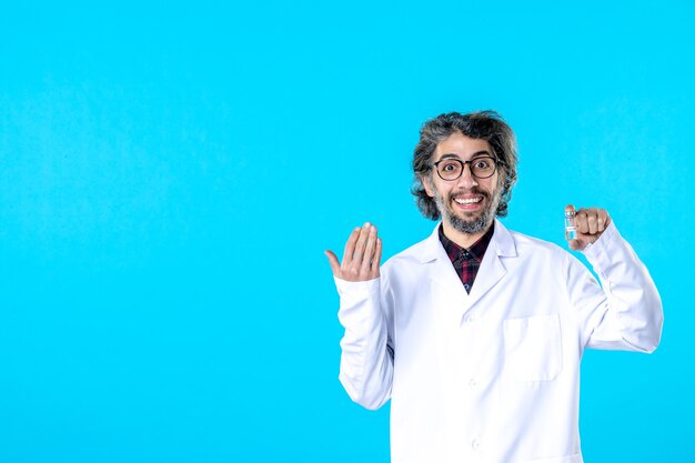 Vista frontal médico de sexo masculino en uniforme médico sosteniendo pequeño frasco en el azul