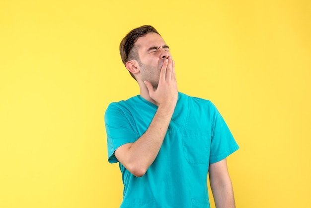 Vista frontal del médico varón bostezando en la pared amarilla