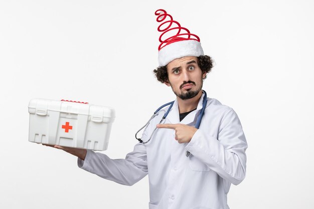 Vista frontal del médico varón con botiquín de primeros auxilios en la pared blanca