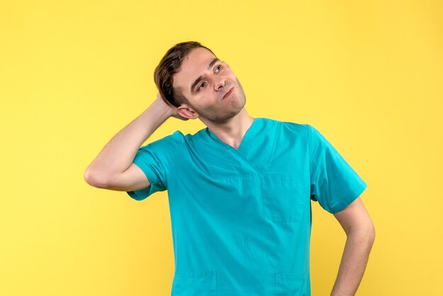 Vista frontal del médico varón con cara estresada en pared amarilla