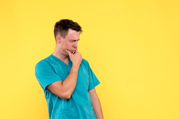 Vista frontal del médico varón con cara de pensamiento en la pared amarilla