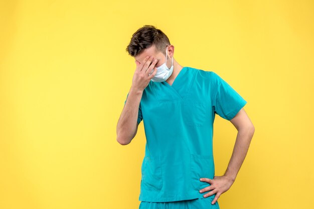 Vista frontal del médico varón con dolor de cabeza en la pared amarilla