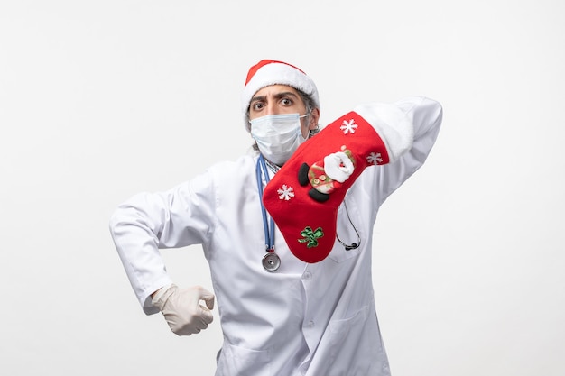 Vista frontal médico varón con gran calcetín rojo sobre piso blanco virus covid- vacaciones de navidad