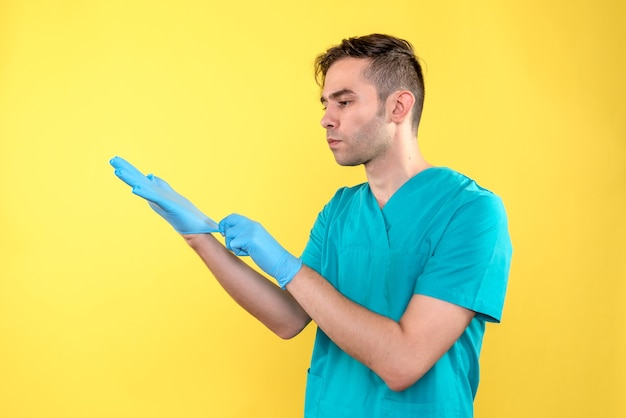 Vista frontal del médico varón con guantes azules en la pared amarilla