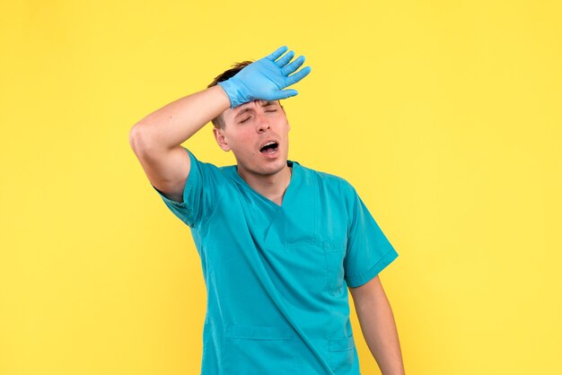 Vista frontal del médico varón con guantes azules en la pared amarilla