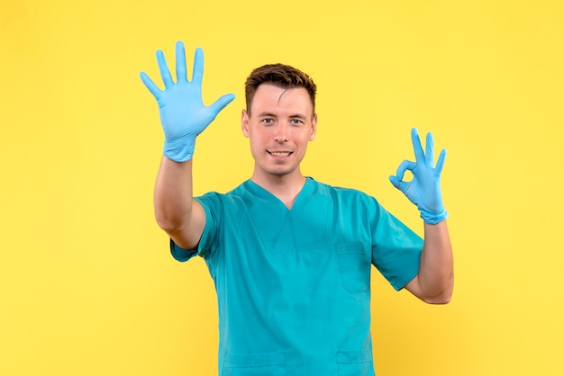 Vista frontal del médico varón con guantes azules en la pared amarilla