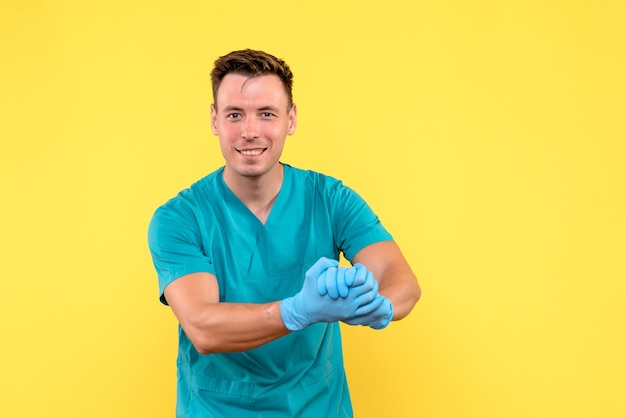 Vista frontal del médico varón con guantes azules en la pared amarilla