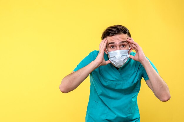 Vista frontal del médico varón con máscara estéril en pared amarilla