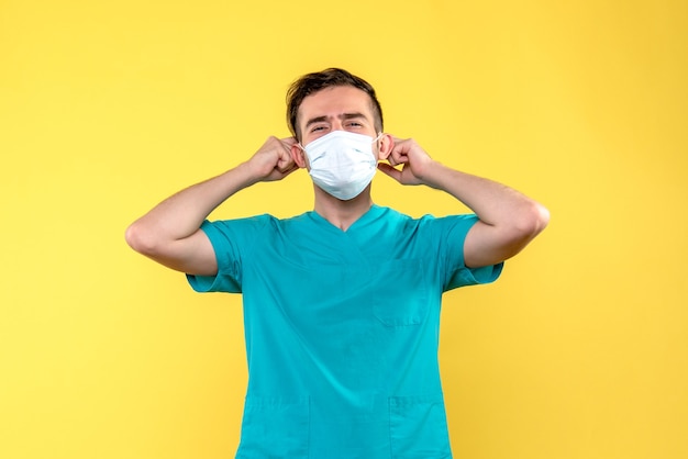 Vista frontal del médico varón con máscara estéril en pared amarilla