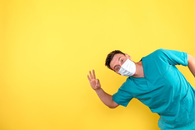 Vista frontal del médico varón con máscara estéril en pared amarilla