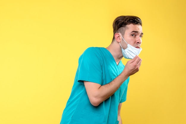 Vista frontal del médico varón con máscara estéril en pared amarilla