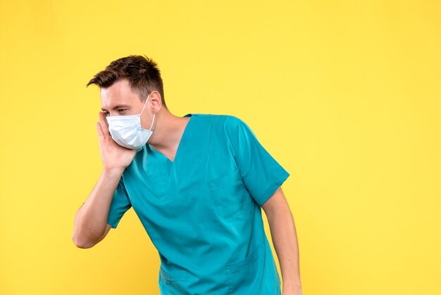 Vista frontal del médico varón con máscara estéril en pared amarilla