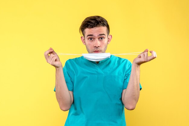 Vista frontal del médico varón con máscara estéril en pared amarilla