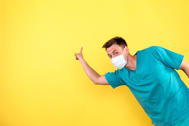 Vista frontal del médico varón con máscara estéril en pared amarilla