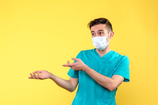 Vista frontal del médico varón con máscara estéril en pared amarilla