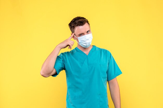 Vista frontal del médico varón con máscara estéril en pared amarilla