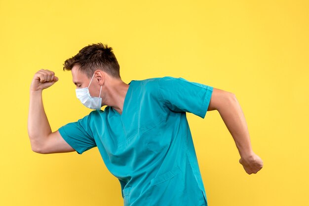 Foto gratuita vista frontal del médico varón con máscara flexionando sobre pared amarilla