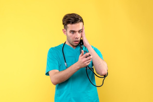 Vista frontal del médico varón midiendo su presión sobre la pared amarilla