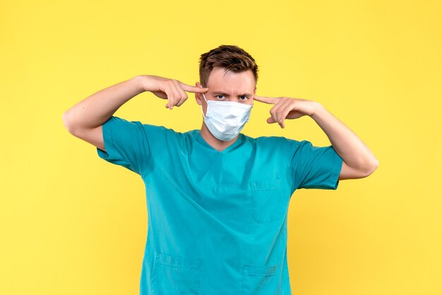 Vista frontal del médico varón pegarse las orejas en la pared amarilla