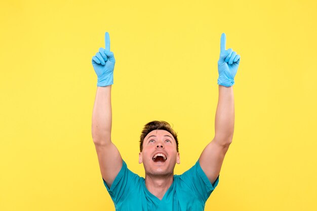 Vista frontal del médico varón posando con guantes azules en la pared amarilla