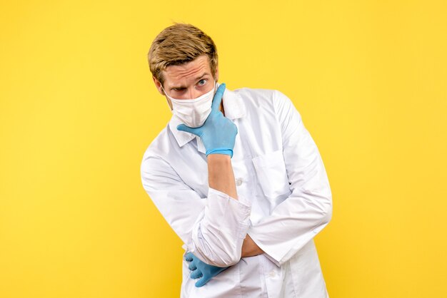 Vista frontal médico varón posando sobre fondo amarillo médico pandémico salud covid- virus
