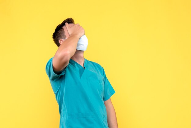 Vista frontal del médico varón que cubre su rostro en la pared amarilla