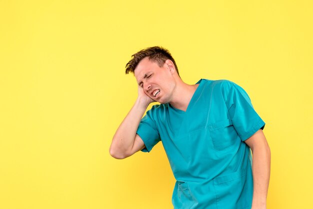 Vista frontal del médico varón que sufre de dolor de cabeza en la pared amarilla
