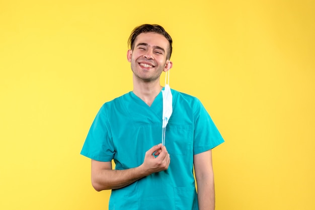 Vista frontal del médico varón quitándose la máscara en la pared amarilla