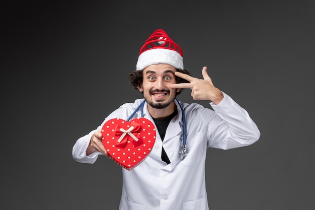 Vista frontal del médico varón con regalo de vacaciones en la pared oscura