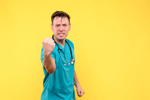 Vista frontal del médico varón regocijándose emocionalmente en la pared amarilla