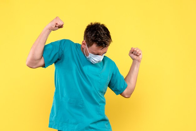 Vista frontal del médico varón regocijándose con máscara en la pared amarilla