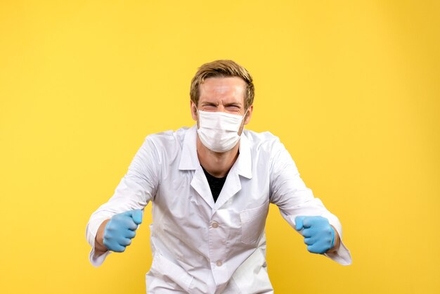 Vista frontal médico varón regocijándose en máscara sobre fondo amarillo pandemia covid- virus de salud