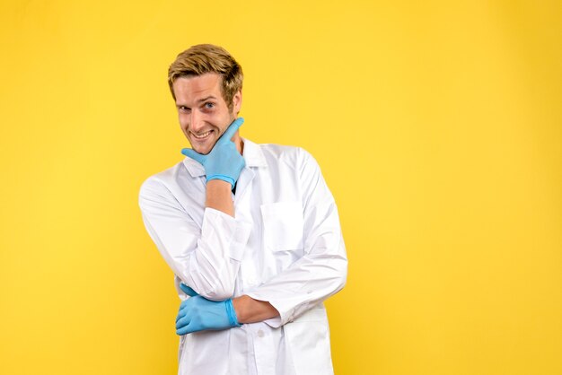 Vista frontal médico varón sonriendo sobre fondo amarillo medic salud covid pandemia