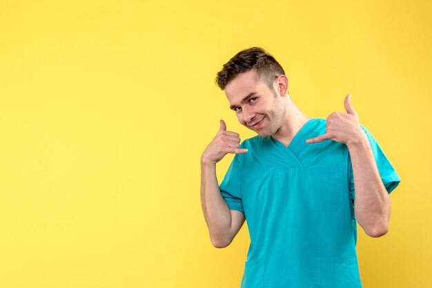 Vista frontal del médico varón sonriendo sobre pared amarilla