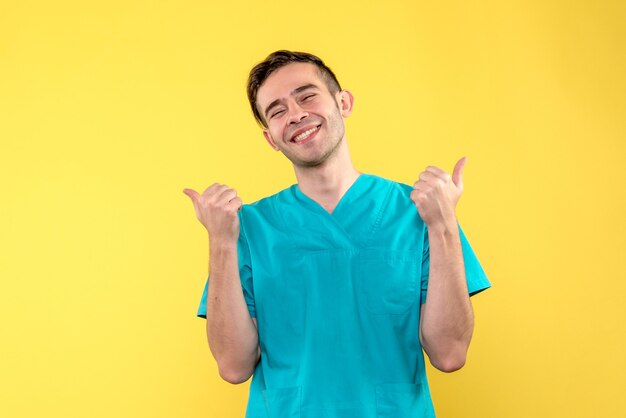 Vista frontal del médico varón sonriendo sobre pared amarilla