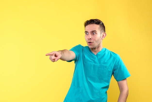 Vista frontal del médico varón sorprendido y emocionado en la pared amarilla